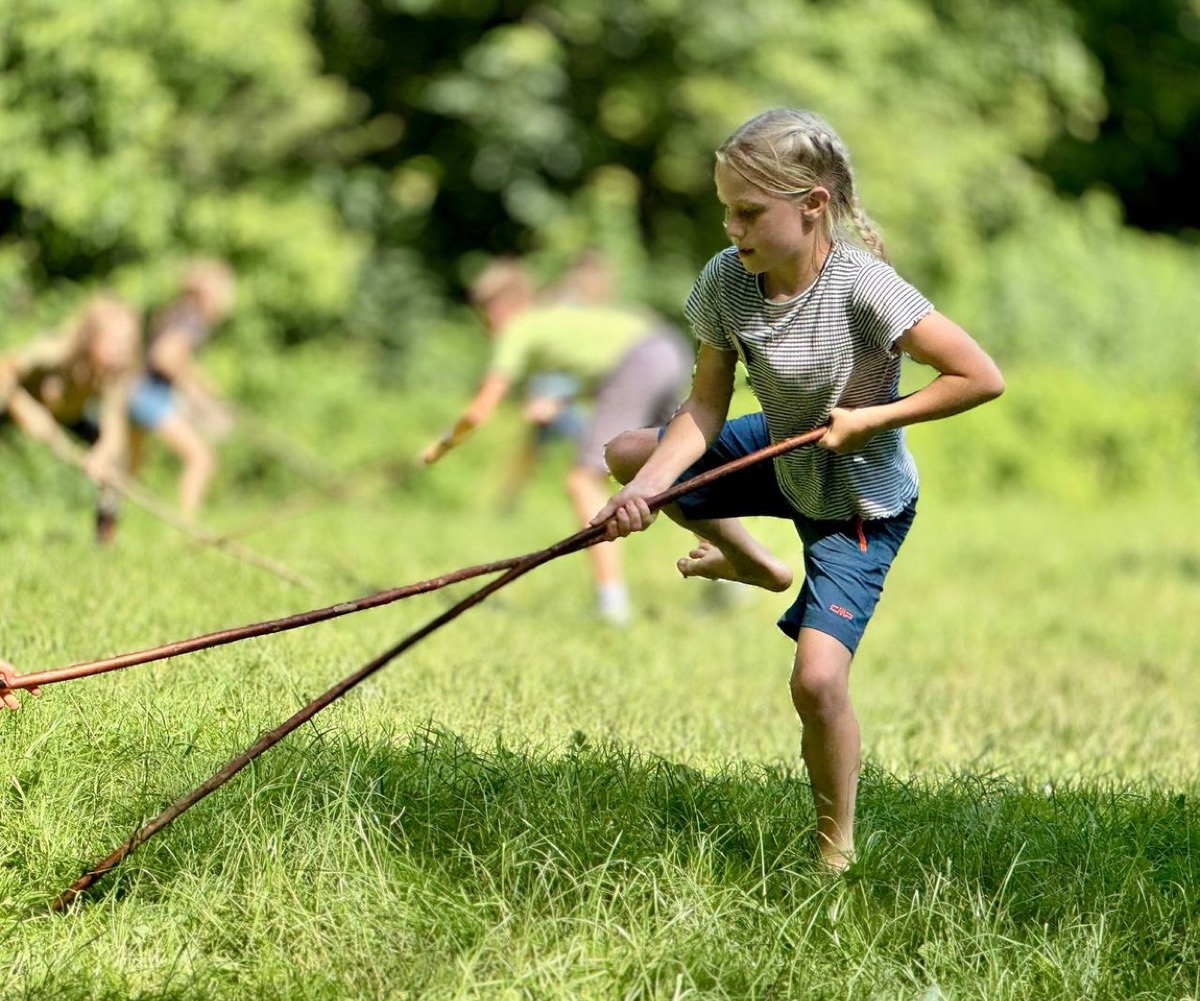 Mädchen spielt mit Stöcken auf der Sommerwiese